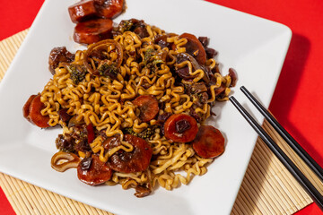 Um prato branco com uma porção de yakisoba de legumes com molho de soja. Yakisoba vegetariano dentro de um prato sobre a superfície vermelha.