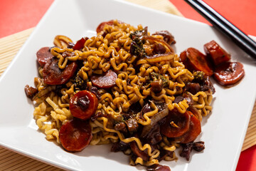 Um prato branco com uma porção de yakisoba de legumes com molho de soja. Yakisoba vegetariano dentro de um prato sobre a superfície vermelha.