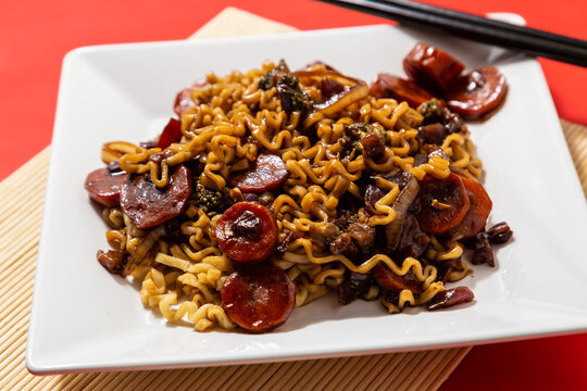Um prato branco com uma por&ccedil;&atilde;o de yakisoba de legumes com molho de soja. Yakisoba vegetariano dentro de um prato sobre a superf&iacute;cie vermelha.