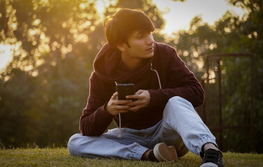 A male student using phone seated on a grass in the city park