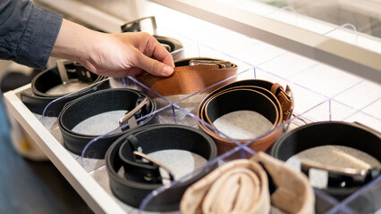 Male hand choosing leather rolled belt from drawer in walk-in closet. Fashion and clothing concept - obrazy, fototapety, plakaty