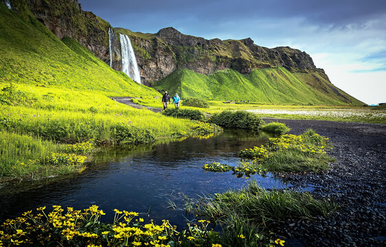Scenic image of Stunning nature in Iceland. two lonely tourists in protective masks walking near the Seljalandsfoss waterfall on vacation, Concept of Traveling During Covid-19 Pandemic isolation