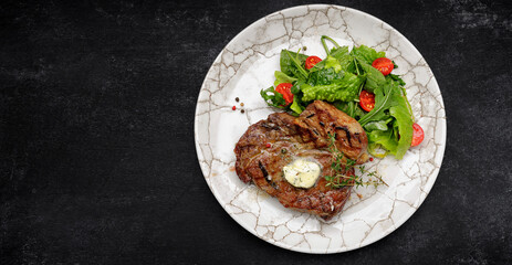 Grilled meat steak with butter, herbs and cherry tomatoes on a white plate, against a dark background