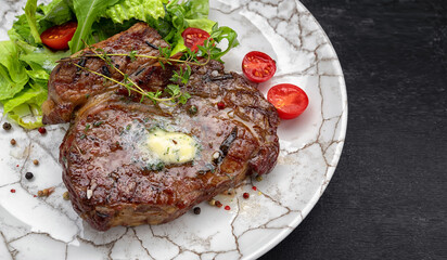 Grilled meat steak with butter, herbs and cherry tomatoes on a white plate, against a dark background