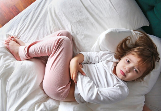 Child in a bed with stomach ache.Caucasian girl with hands on belly. Health disorder concept.