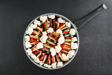 Ratatouille dish of fresh vegetables in a frying pan on a dark background.