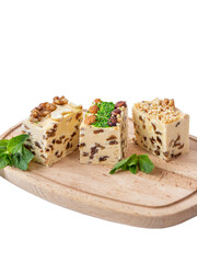 Three pieces of halva with raisins lie on a wooden board. Halva is decorated with walnuts, almonds, pistachios, fresh mint. White background, isolate. National sweets, organic desserts concept