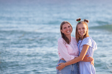 Fototapeta na wymiar Mom and her teenage daughter hugging and smiling together over blue sea view