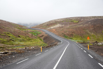 Deserted winding road climbing a mountain shrouded in  clouds in Iceland on a summer day