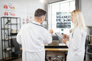 Medical experts in white lab coats writing on flipchart while analysing results of x ray scan. Man and woman having meeting at hospital about severe patient diagnosis.