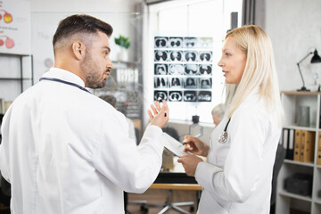 Obraz premium Two qualified doctors in lab coats standing near glass flip chart and talking about results of mri. Colleagues on meeting at conference room. Diagnosis and disease concept.