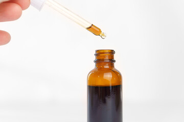 The solution drips from a pipette into a brown bottle on a white background. Cosmetics. Herbal innovative skin care products.
