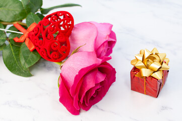 A simple arrangement with a flower and a heart shape decoration. Rose and gift box on marble background.