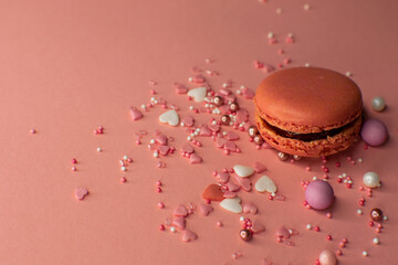 Pinker Macaron vor rosanem Hintergrund mit Zuckerstreuseln in pastell und herzförmigen Streuseln,...