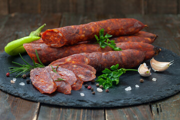 Dry sausages made of pork meat on a black board with fresh herbs and spices.  Smoked, homemade sausage.