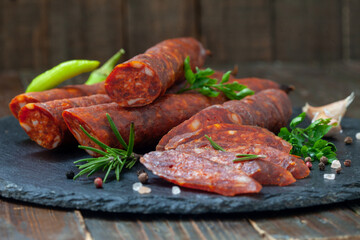 Dry sausages made of pork meat on a rustic, wooden table with fresh herbs and spices.  Smoked, homemade sausage.