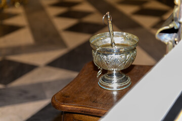 The Sacrament Silver Cup of Holy Water in on a Dark Wooden Table during a ceremony or mass on Catholic church or cathedral interior background