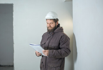 a man in a white construction helmet is standing with documents in a room where repairs or construction.