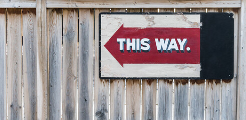 This way red arrow sign on wooden fence background