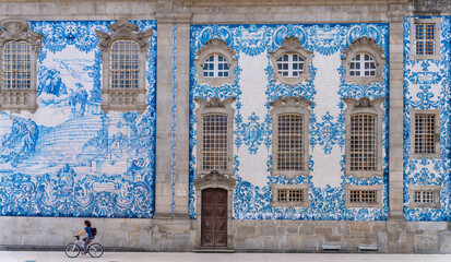 Carmo church in Porto, Portugal, decorated with blue tiles - Traveler woman cycling next to the painted ceramic wall in the old town of Oporto. - obrazy, fototapety, plakaty