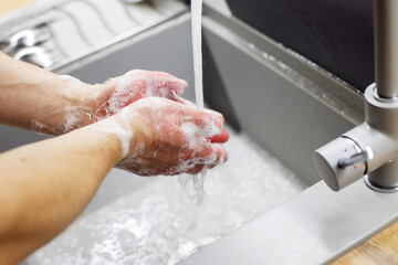 A man washes his hands with soap under the tap under running water close-up. Health, and hygiene concept.