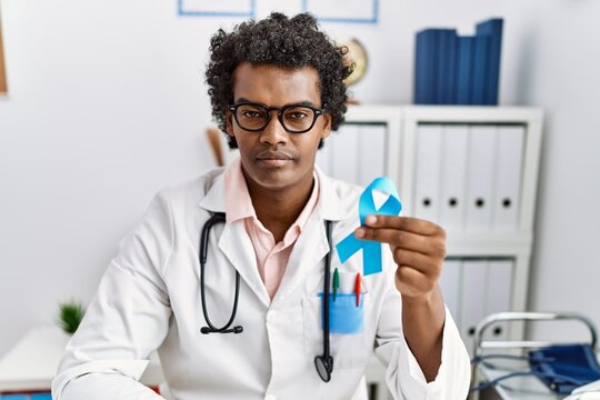 African doctor man holding blue ribbon thinking attitude and sober expression looking self confident