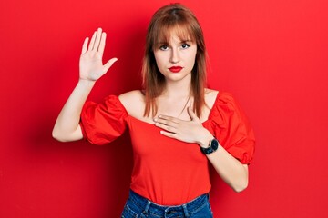 Redhead young woman wearing casual red t shirt swearing with hand on chest and open palm, making a...