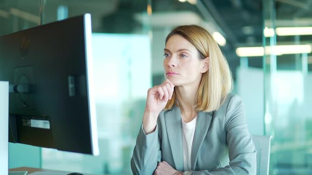 thoughtful focused business woman office worker working at computer desk at workplace in office. Serious confident employee is thinking about solving a problem strategy. female startup founder siting