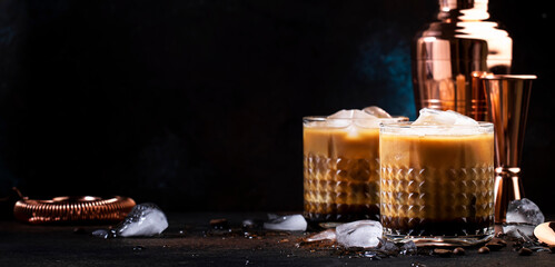 White russian alcoholi cocktail drink with vodka, coffee liqueur, cream and ice, dark table background, bar tools, copy space