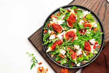 Fresh summer fig salad with white cheese, nuts, arugula and jam dressing on white table background, top view, copy space
