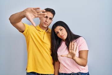 Young couple standing over isolated background doing frame using hands palms and fingers, camera perspective