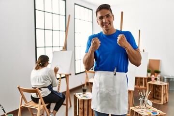 Young hispanic couple at art studio very happy and excited doing winner gesture with arms raised, smiling and screaming for success. celebration concept.