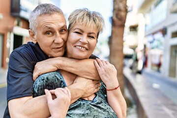 Fototapeta na wymiar Middle age caucasian couple of husband and wife together on a sunny day outdoors. Smiling happy in love hugging at the city.