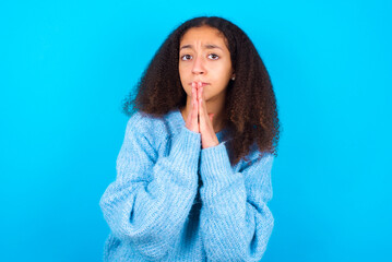 African teenager girl wearing blue sweater over blue background keeps palms pressed together in...