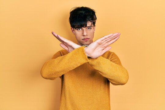 Handsome hipster young man wearing casual yellow sweater rejection expression crossing arms and palms doing negative sign, angry face