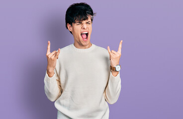 Handsome hipster young man wearing casual winter sweater shouting with crazy expression doing rock symbol with hands up. music star. heavy concept.