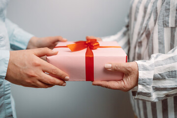 Person hand giving pink gift box with red ribbon to a woman.