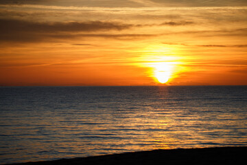 Obraz premium Calm Ionian sea with sunset sky and sun through the clouds over in Puglia, Italy. Meditation sea and sky background. Tranquil seascape with horizon over the water