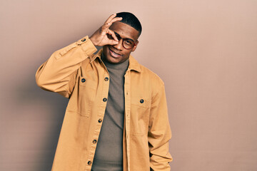 Young black man wearing casual clothes and glasses smiling happy doing ok sign with hand on eye looking through fingers