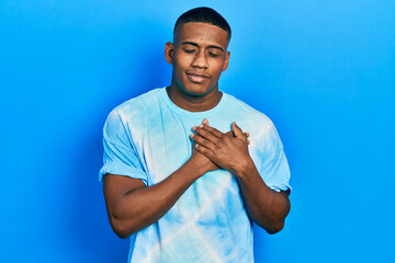 Young black man wearing tye die t shirt smiling with hands on chest with closed eyes and grateful gesture on face. health concept.