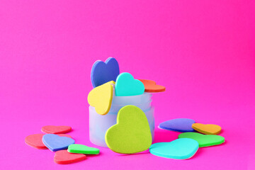 Love, Valentine's day. Colored hearts inside a small container and scattered on a pink background.
