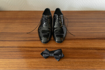 Patent leather groom shoes and bowtie over wooden furniture getting ready concept, horizontal image