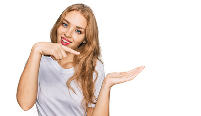 Young caucasian girl wearing casual white t shirt amazed and smiling to the camera while presenting with hand and pointing with finger.