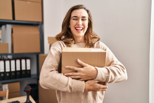 Young woman ecommerce business worker hugging package at office