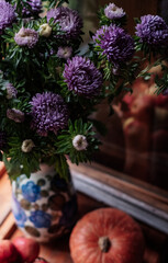 A bouquet of lilac asters, a pumpkin and garden apples on a wooden windowsill