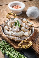 White tiger shrimps, raw prawns in a skillet with rosemary. Wooden background. Top view