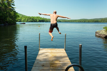 Happy man jumping off dock into lake the summer time. Having fun on vacation.