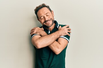 Middle age man wearing casual clothes hugging oneself happy and positive, smiling confident. self...