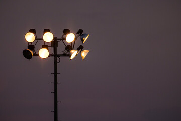 Stadium light pole holding many light fixtures against a dark moody sky