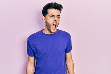 Obraz premium Young hispanic man wearing casual t shirt angry and mad screaming frustrated and furious, shouting with anger. rage and aggressive concept.